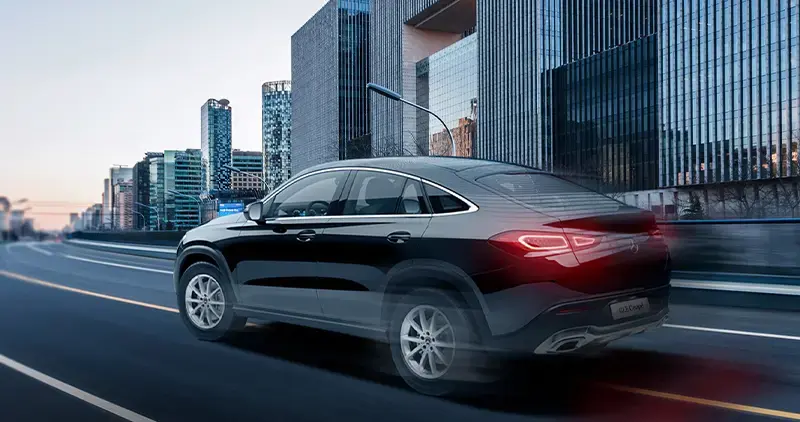 Vehículo Mercedes-Benz GLE Coupé negro conduciendo por avenida urbana con edificios de fondo.