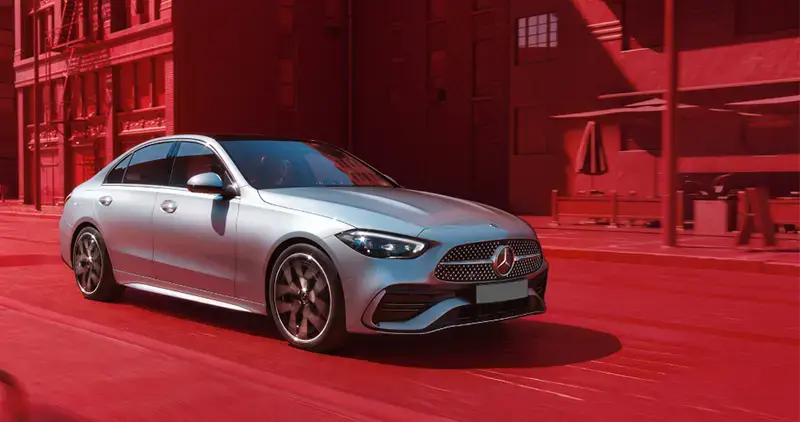 Vehículo Mercedes-Benz plateado circulando en una ciudad con fondo rojo.