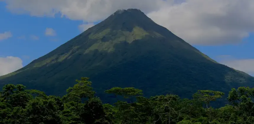 Vista del majestuoso Volcán Arenal rodeado de vegetación tropical bajo un cielo parcialmente nublado
